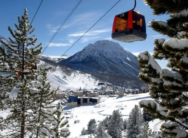 Snow-covered mountain and a cable car in a winter landscape with trees and buildings.