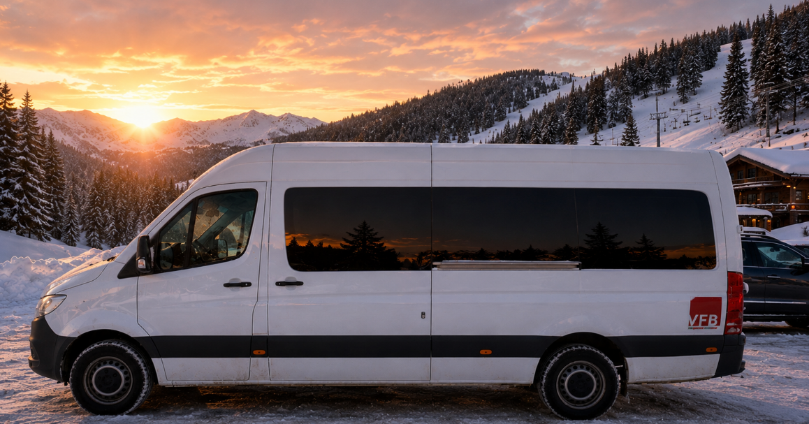 A white passenger van parked on snow with a scenic mountain landscape and sunset in the background.