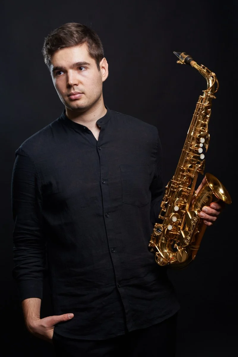 Junger Mann hält ein goldfarbenes Saxophon vor einem schwarzen Hintergrund.