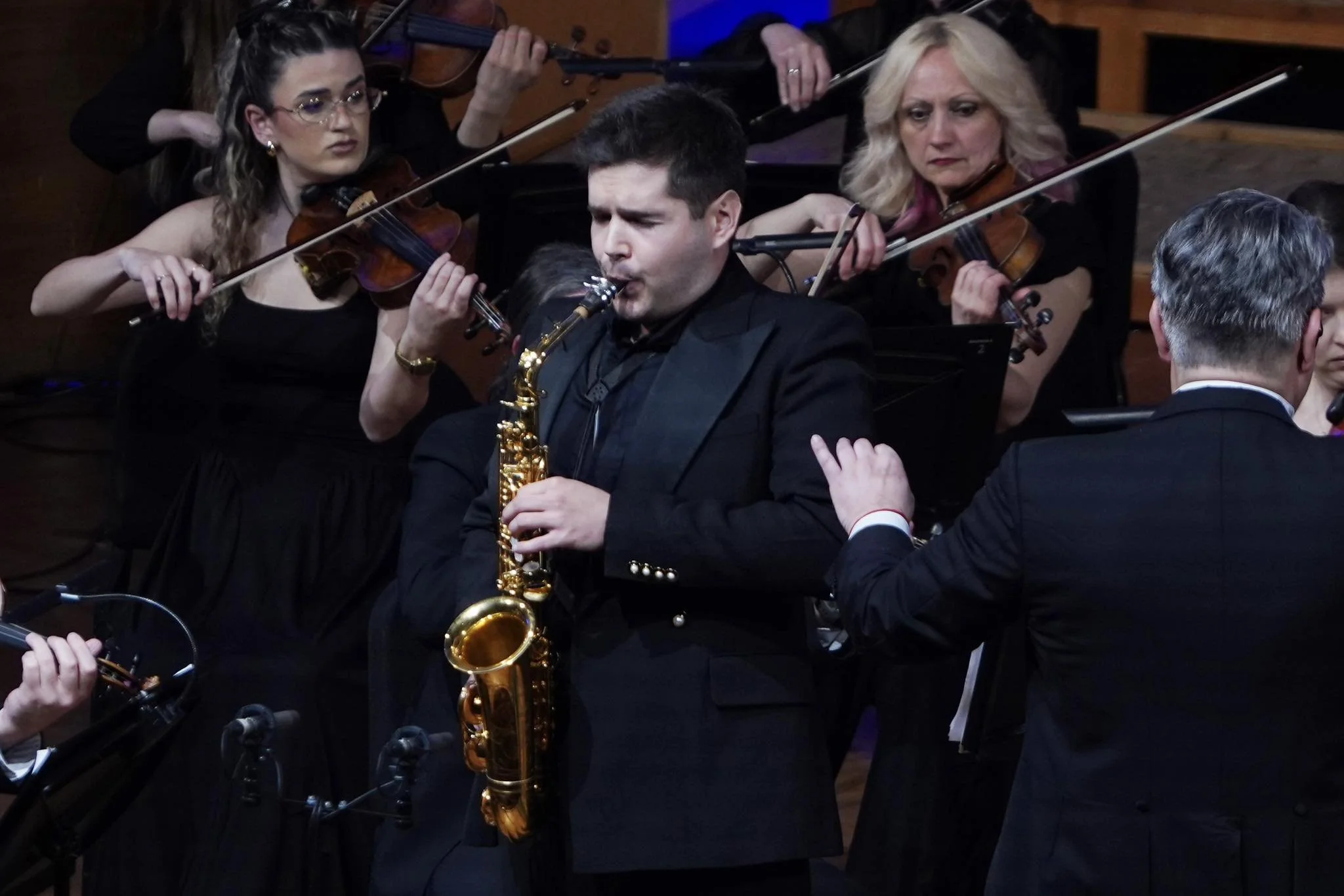 Orchestermusiker, darunter ein Saxofonspieler und mehrere Geiger, während eines Auftritts in einem Konzertsaal.