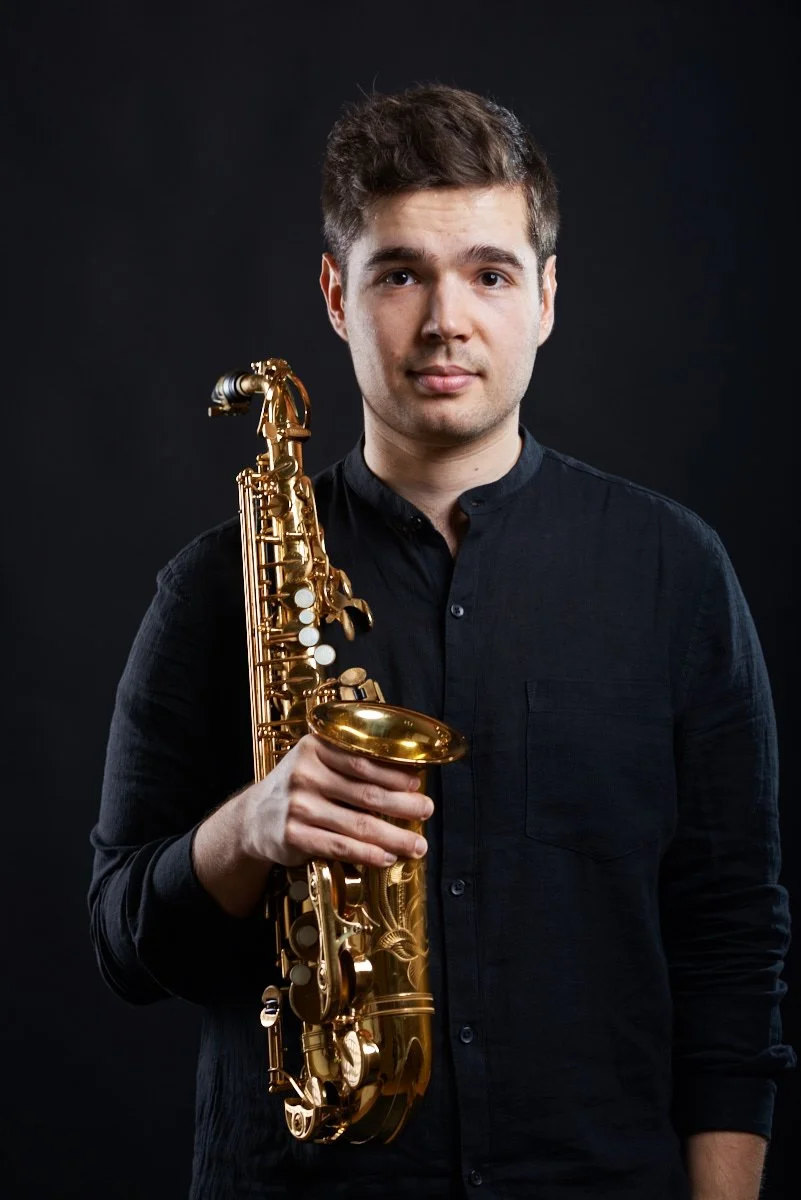 Junge Mann mit dunklem Hemd hält eine goldene Saxophon vor schwarzem Hintergrund.