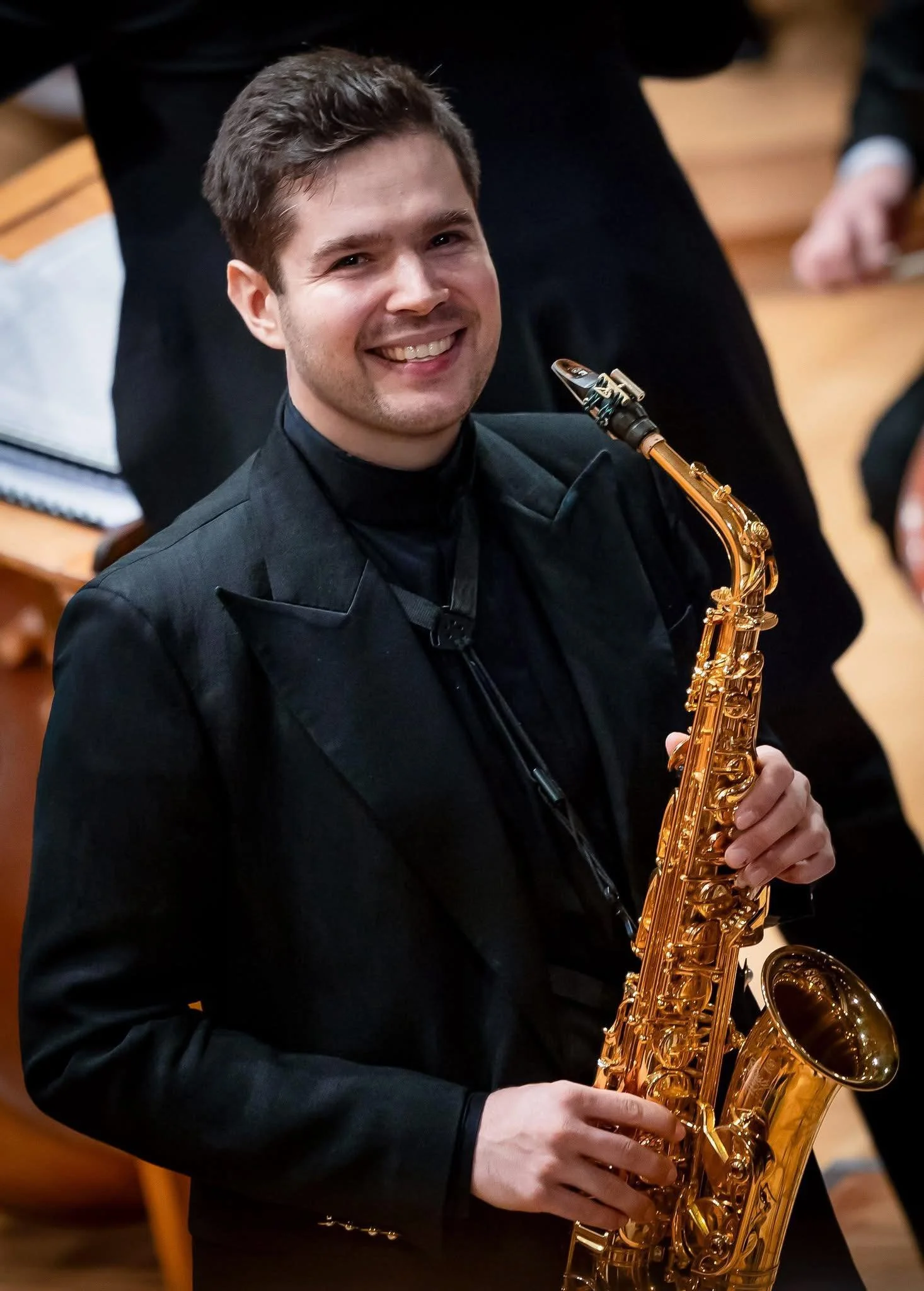 Junger Mann mit dunklem Anzug spielt Saxophon in einem Orchester.