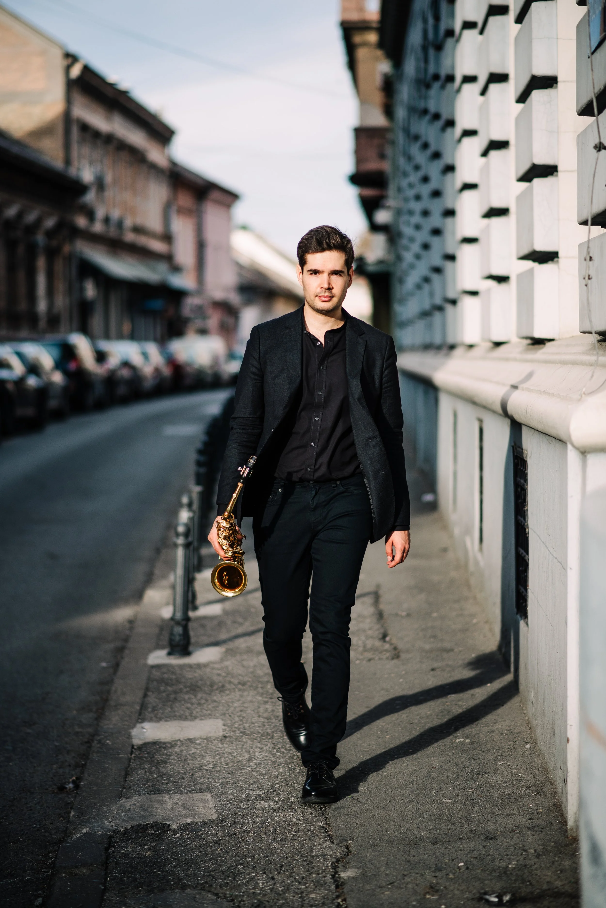Ein junger Mann in dunkler Kleidung läuft mit einer goldenen Saxofon auf einer Stadtstraße.