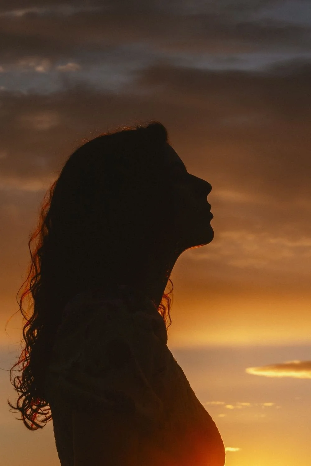 Silhouette of a person gazing upward against a warm sunset sky, conveying reflection, presence, and a quiet moment of inner awareness.