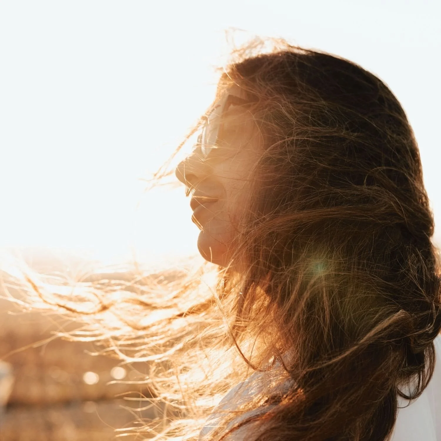 Woman standing outdoors with sunlight and wind flowing through her hair, embodying experiential wellness, resilience, and a balanced mind body health approach.