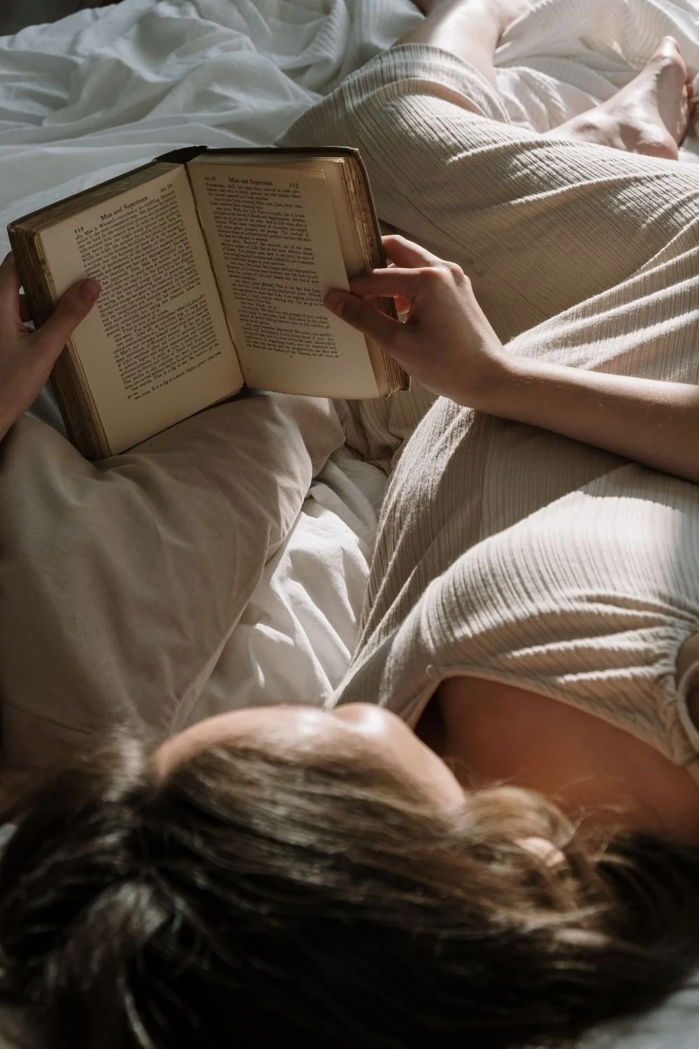 Person relaxing in bed while reading a book in soft natural light, reflecting the self-reflection and embodiment practices that support deeper body based awareness.