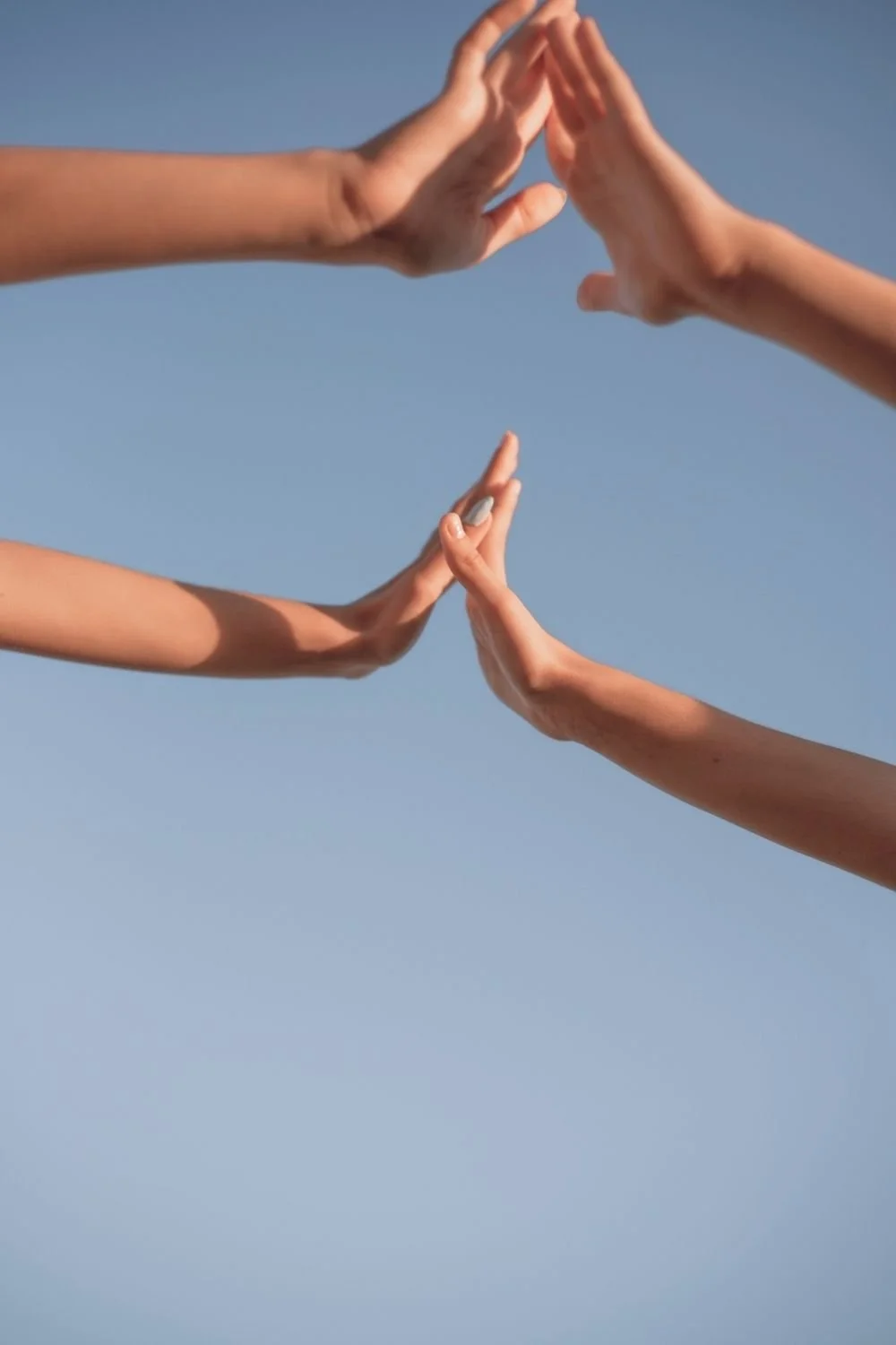 Four hands reaching toward one another against a clear blue sky, symbolizing connection, support, and somatic healing practices used in somatic therapy online and somatic practices for nervous system regulation.