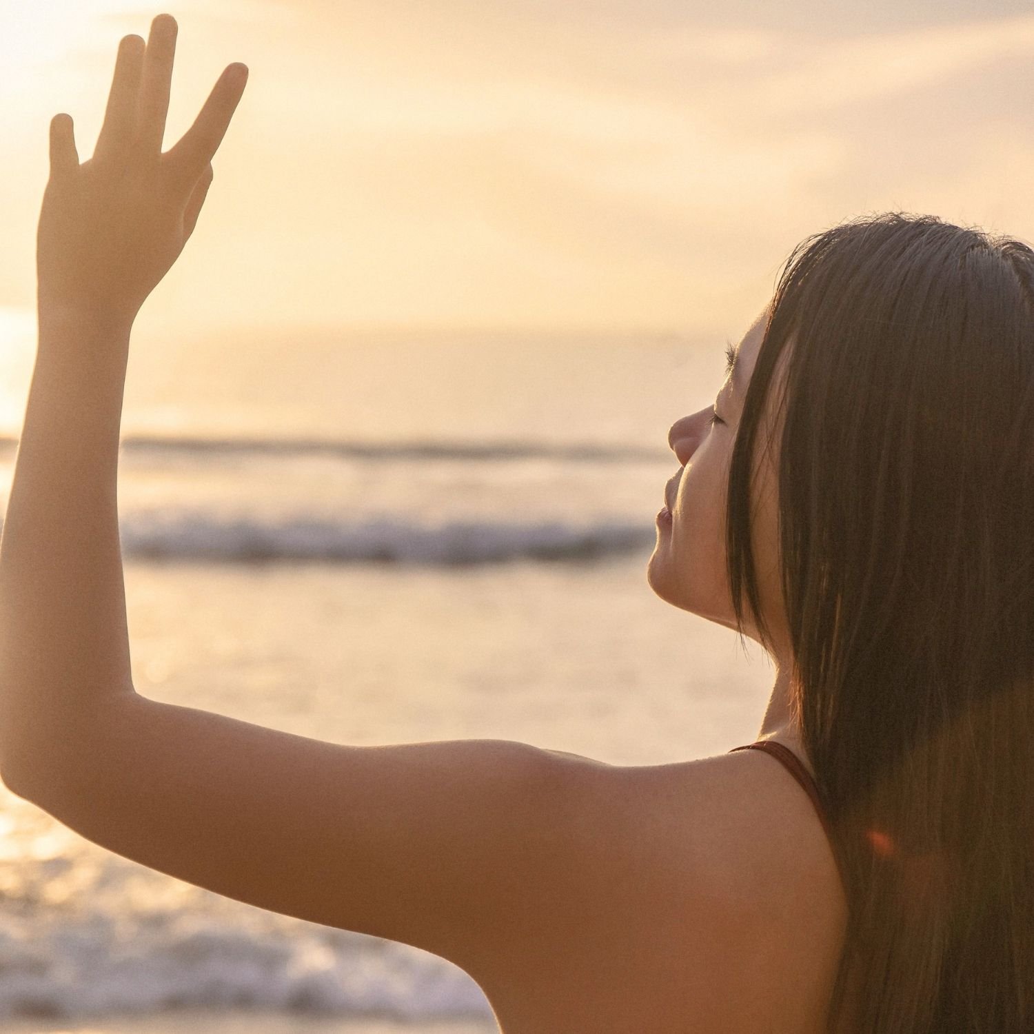 Person raising a hand toward the sunset by the ocean, embodying the principles of The Conscious Body Method™ through mindfulness, embodiment practices, conscious body recovery, and mind body healing.