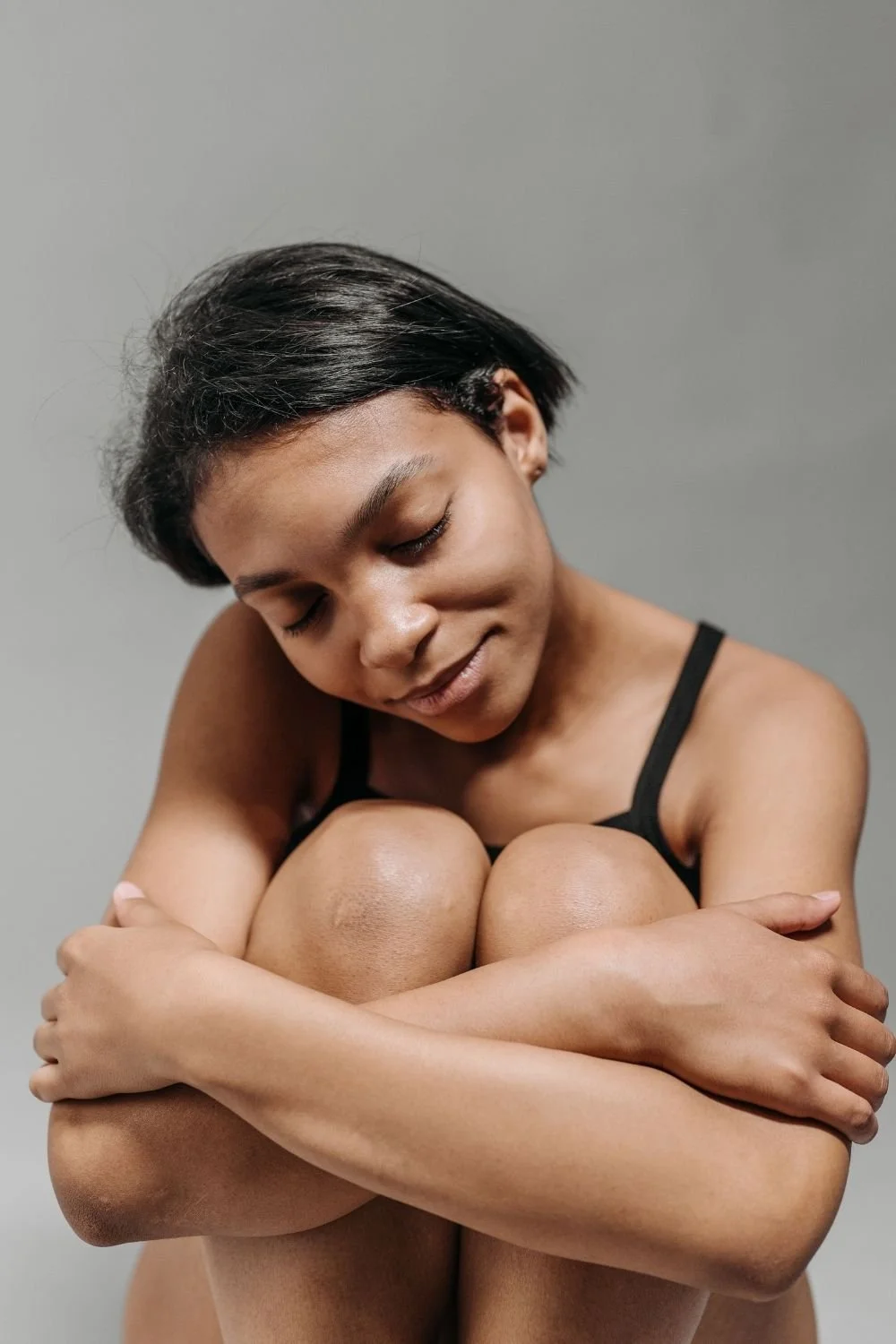 Person sitting with arms wrapped around their knees in a gentle self-hug, illustrating body based awareness, emotional resilience, and healing from self sabotage patterns.