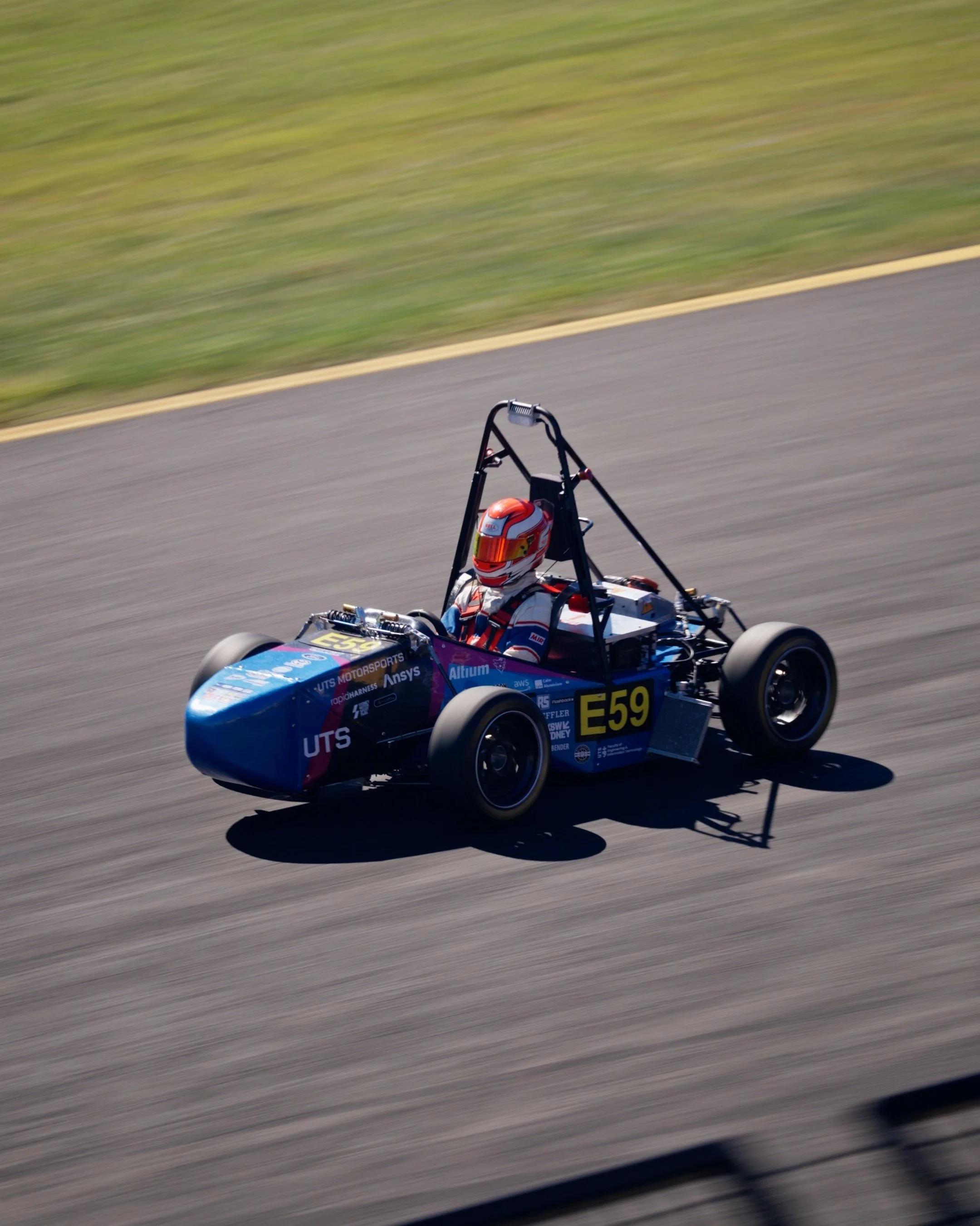 Race car driver wearing helmet and racing suit driving a race car on a track, with motion blur background.