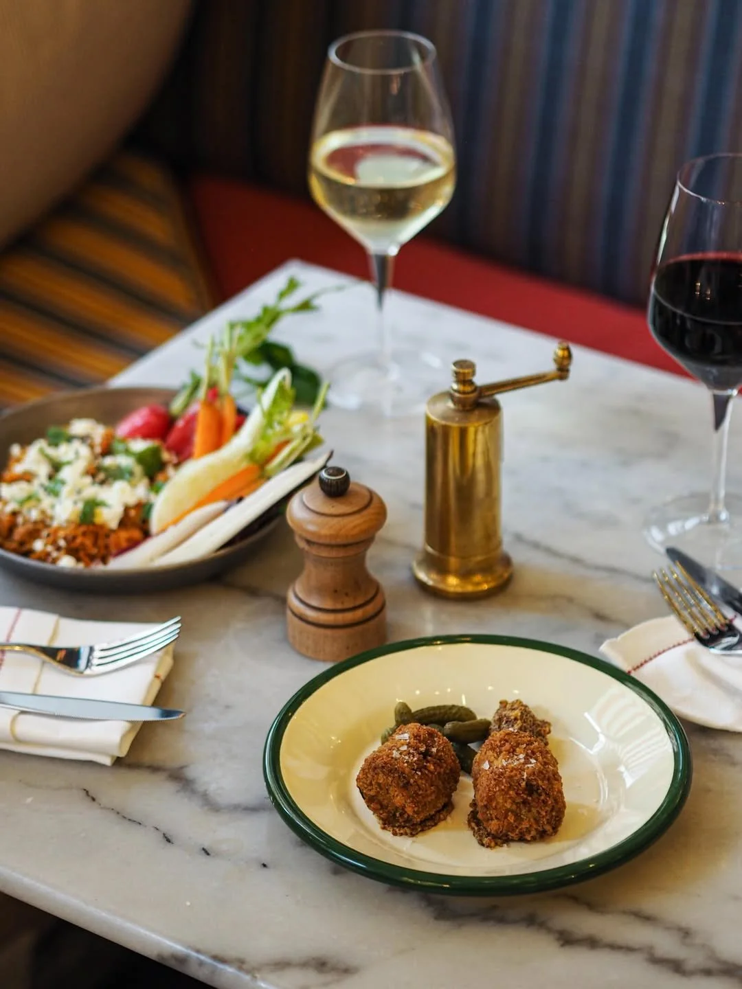 A restaurant table with two wine glasses filled with white and red wine, a plate of fried appetizers, a bowl of salad, and salt and pepper shakers.