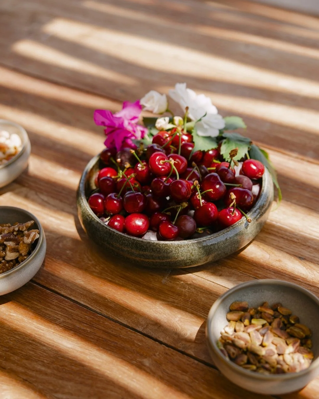 A bowl of fresh red cherries on a wooden table, decorated with pink and white flowers.