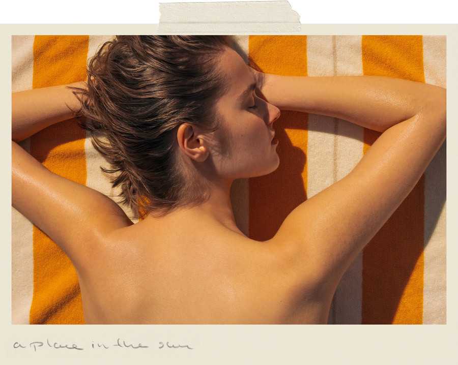 A woman lying on her side on a striped orange and white towel, soaking up the sun with her eyes closed and arms resting above her head.