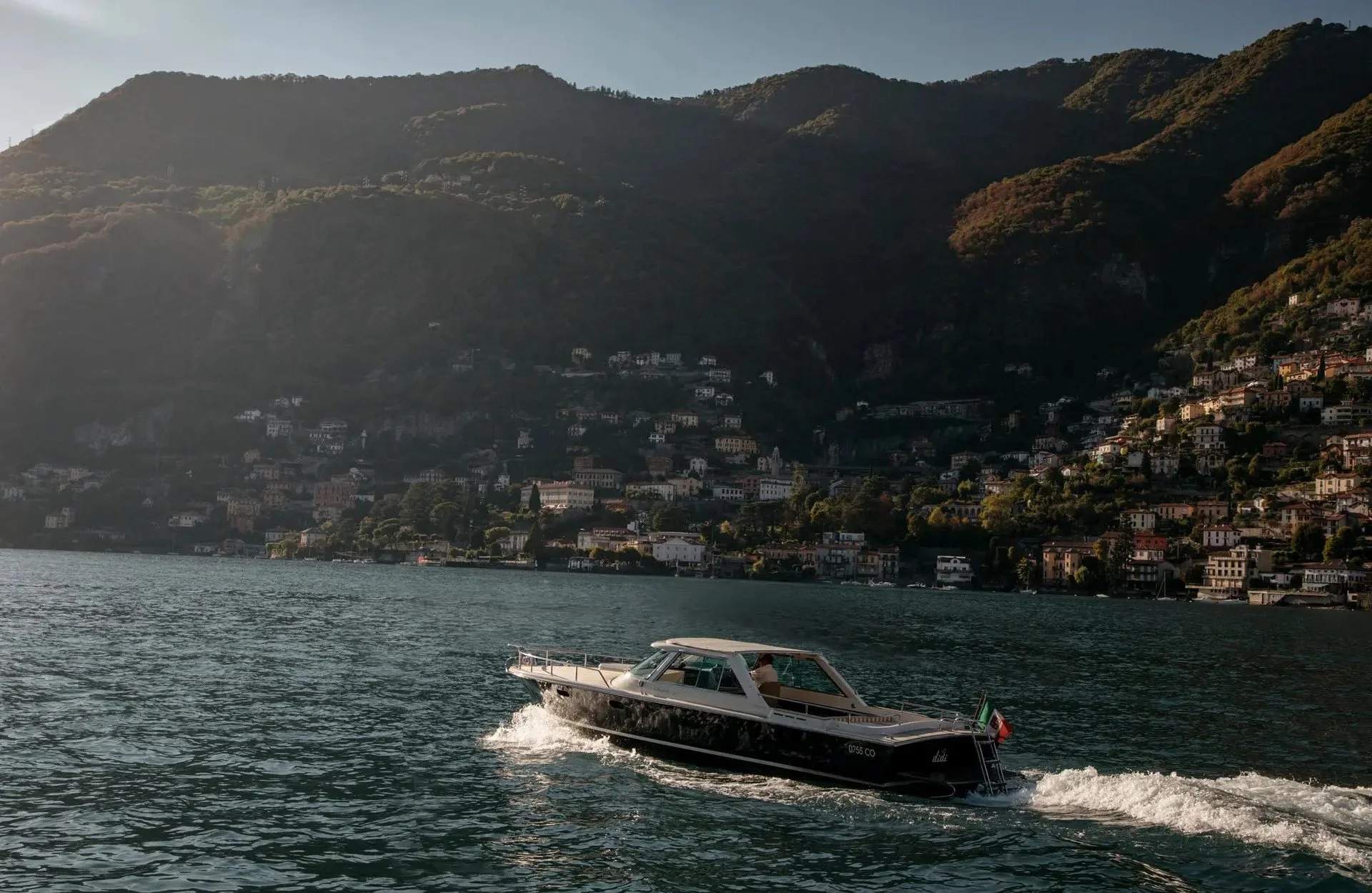 A boat on a lake with a hillside town in the background.