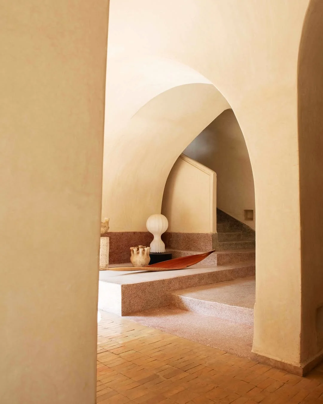 Interior view of a space with curved architecture and earthy tones, displaying decorative ceramics and a wooden tray on a stepped surface.