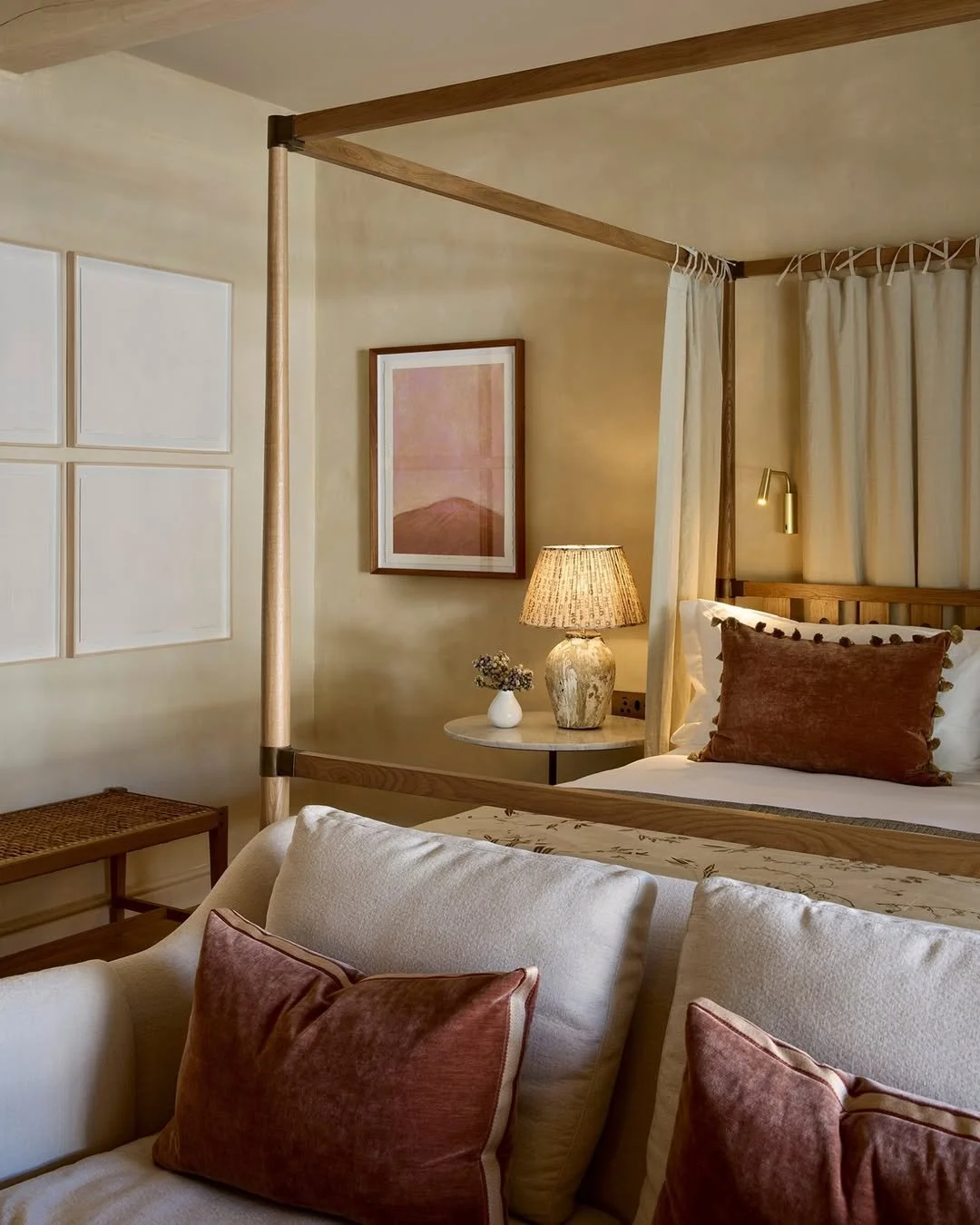 A cozy bedroom with a four-poster bed, pillows, a bedside lamp, and a framed picture on the wall.