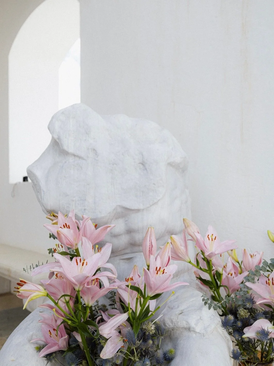 A white sculpture with pink lilies and other flowers in front.