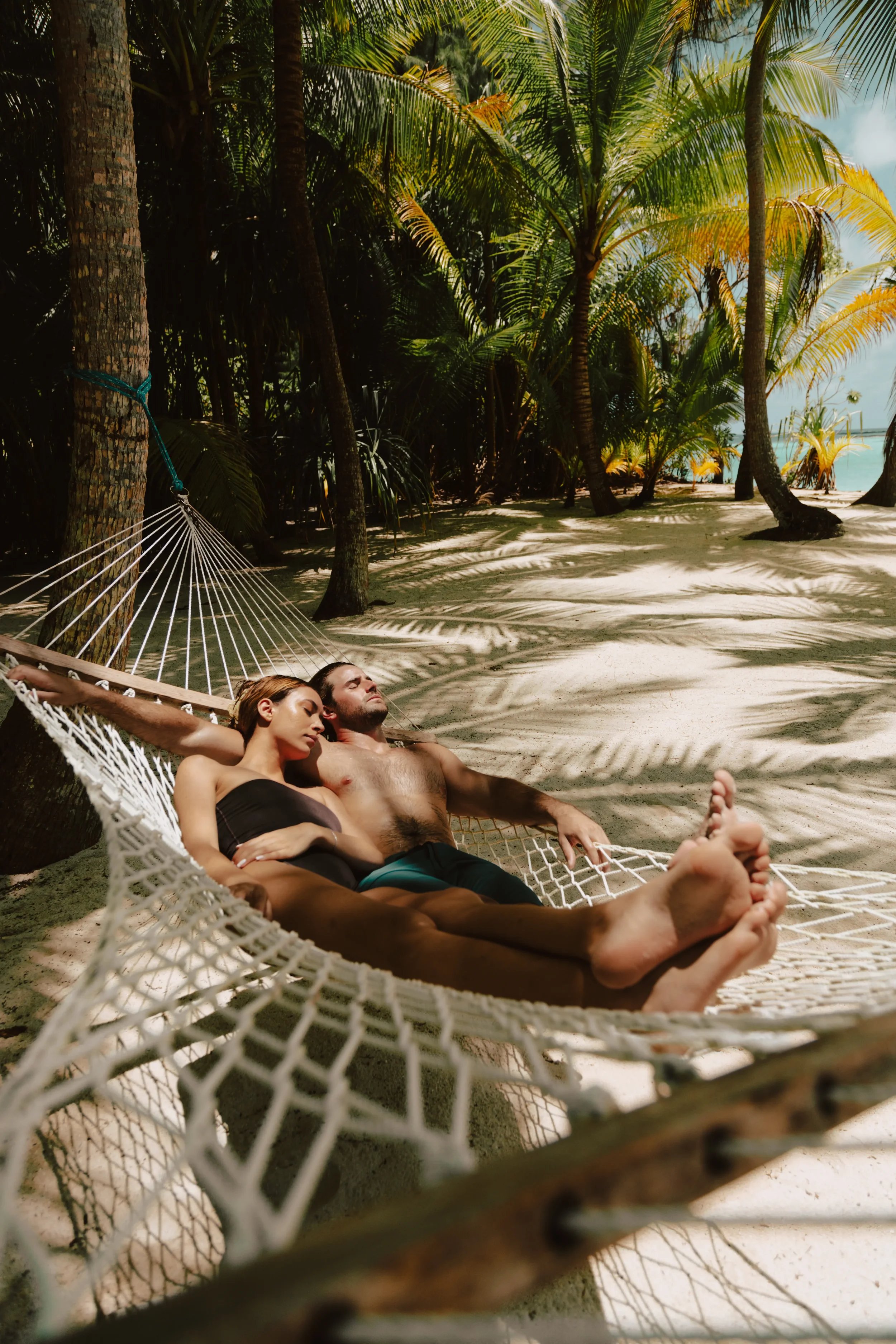 A couple relaxing in a hammock on a beach surrounded by palm trees.