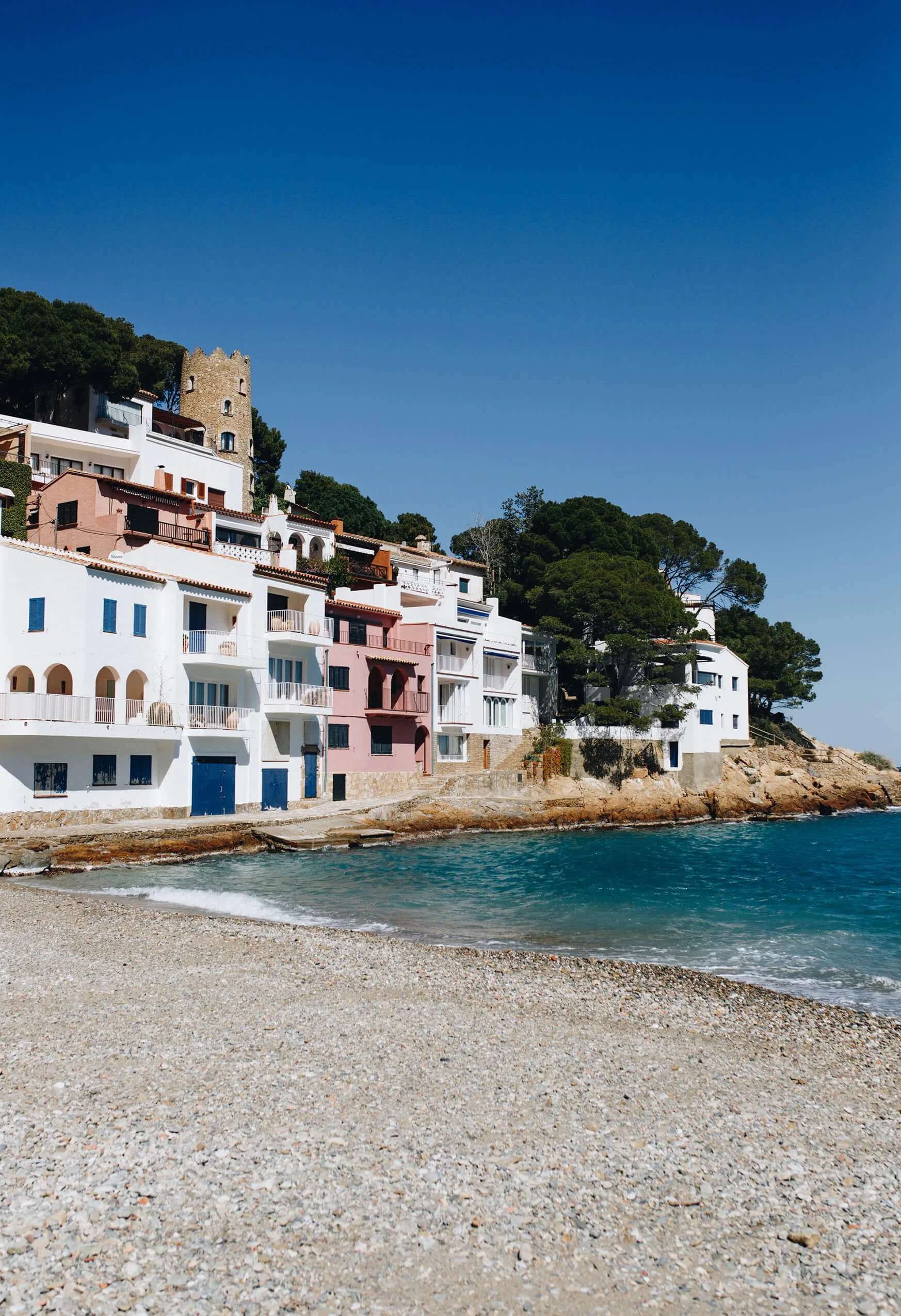 Colorful buildings and houses on a hillside next to the ocean, with a small sandy beach and clear blue sky.