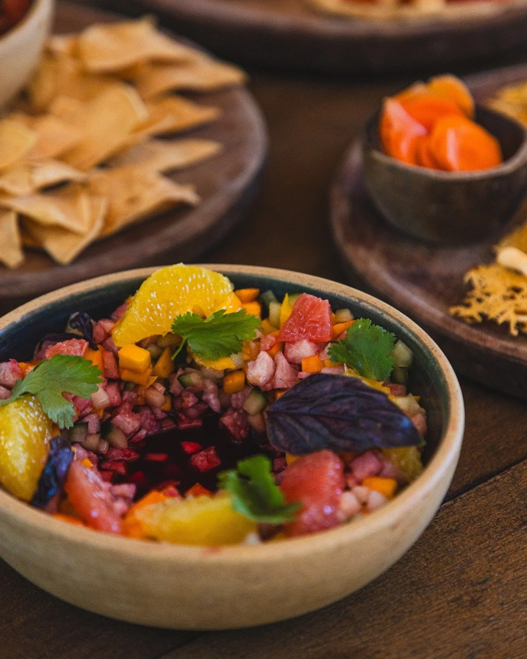 A bowl of colorful chopped fruit salad with citrus slices and cilantro, surrounded by various small bowls of chips and salsa.