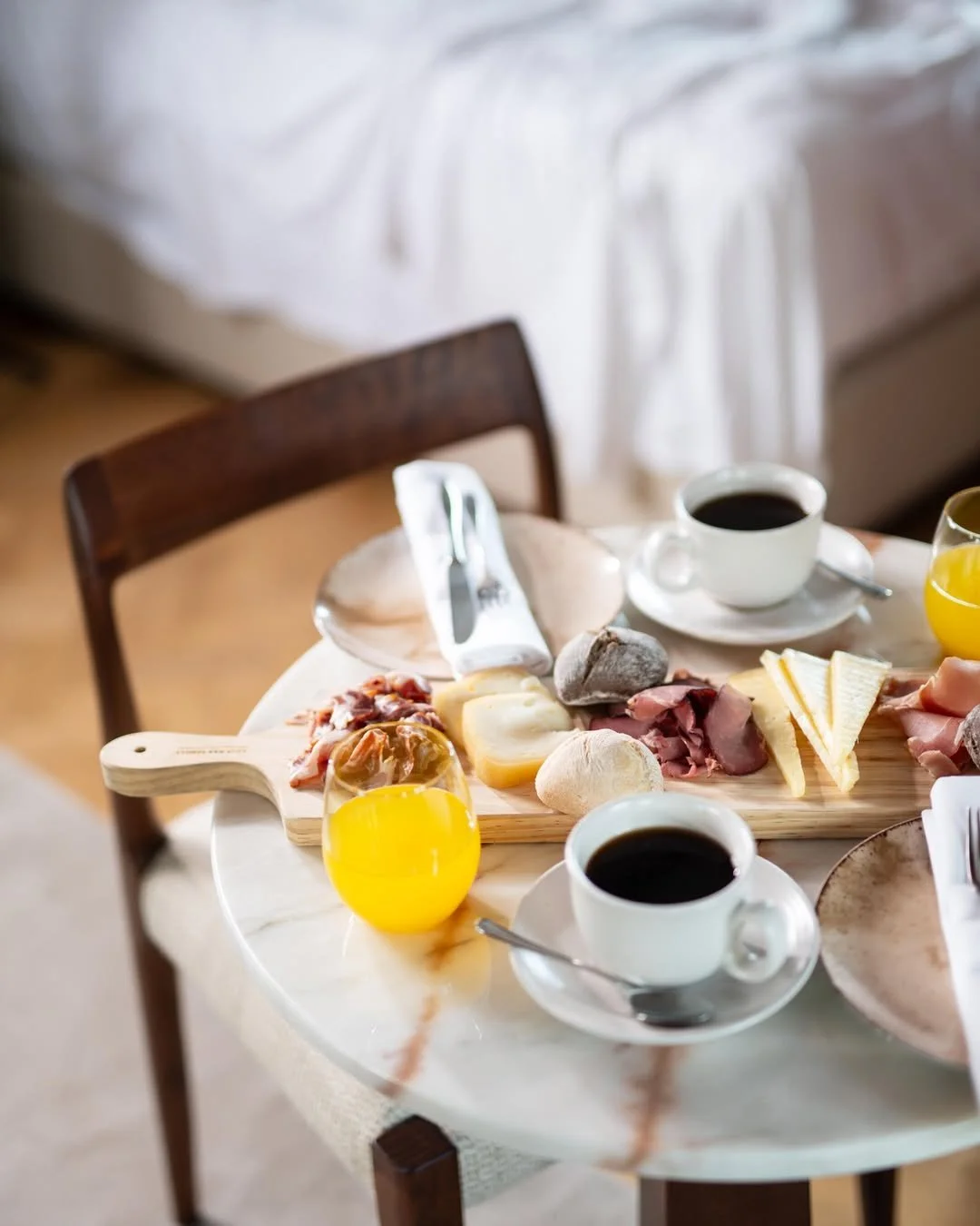 A breakfast table with coffee, orange juice, cheese, cold cuts, and pastries.