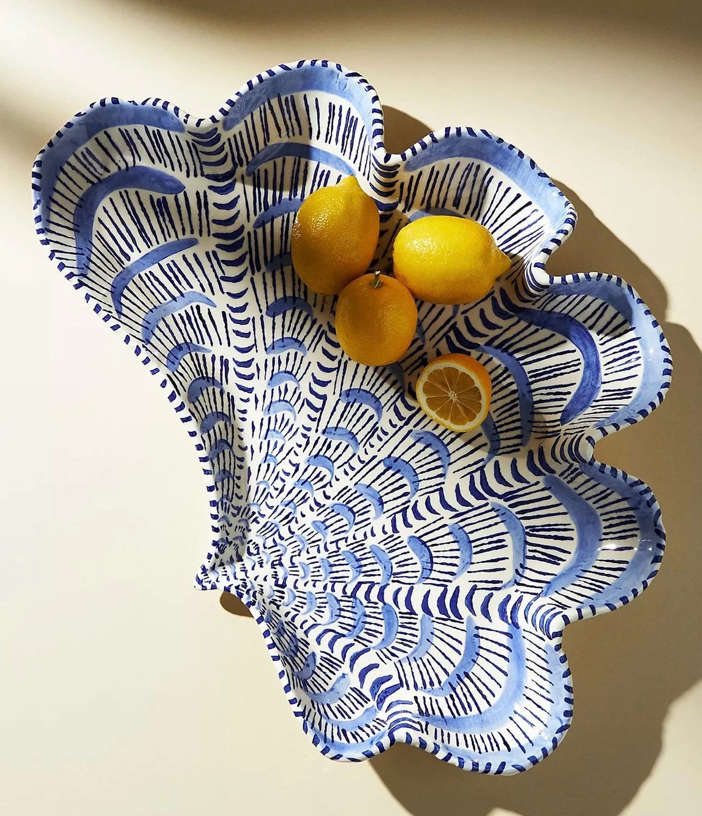 Decorative blue and white ceramic bowl with scalloped edges, holding three yellow lemons and one lemon half, on a white surface