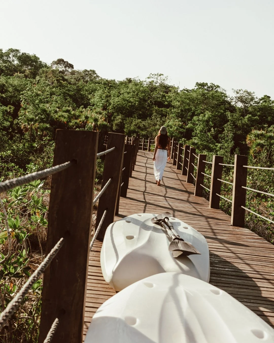 A person walking on a wooden bridge surrounded by green trees, with a white helmet and harness resting on the bridge in the foreground.