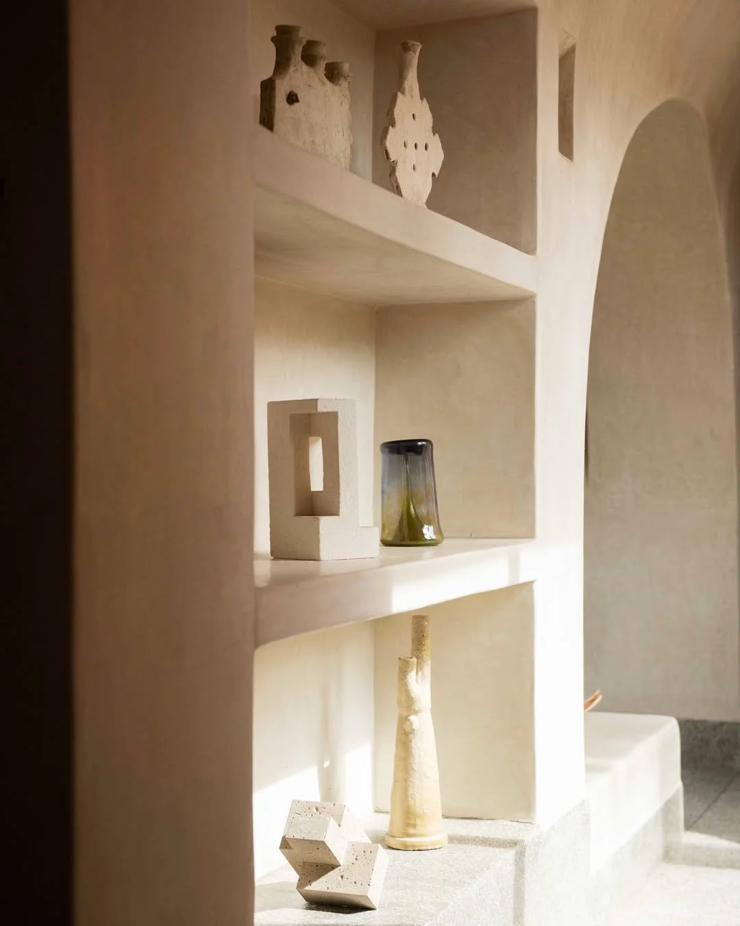 Minimalist built-in wall shelves with ceramic and glass art objects, including vases and decorative figures, illuminated by soft natural light.