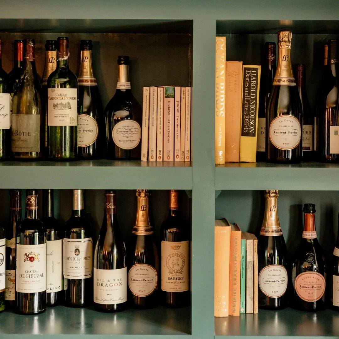 Bathroom shelf with various bottles of champagne and wine along with some books.