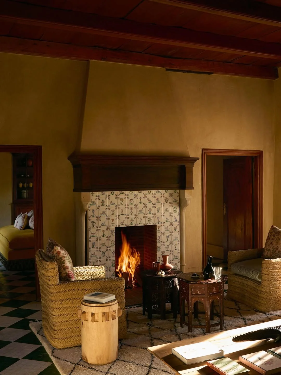 Living room with a lit fireplace, two armchairs, a side table with books, and a coffee table with decorative items.