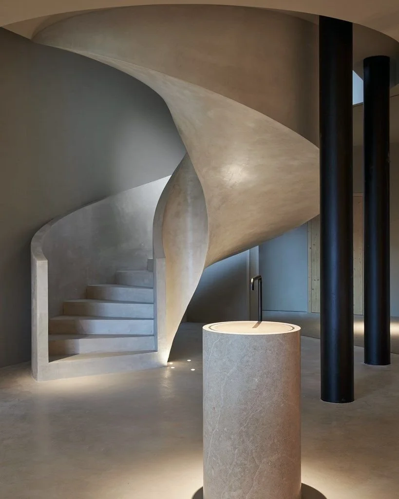 Modern interior with a spiral staircase, cylindrical stone basin with a black faucet, and black columns.