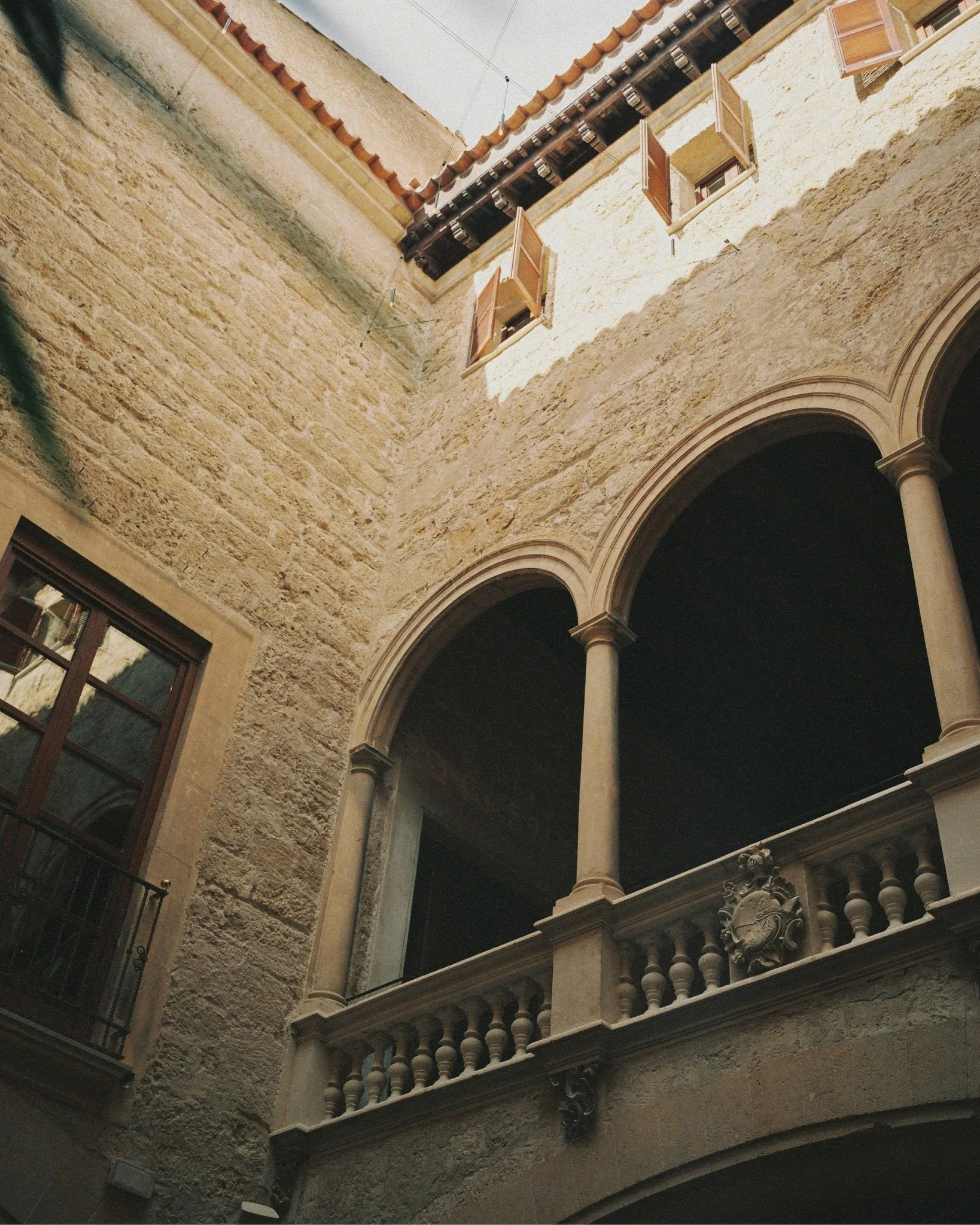 View of a stone building with open windows and a decorative balcony with columns, taken from below upwards.