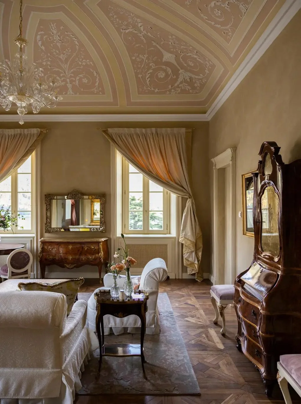 Elegant living room with high ceilings, ornate moldings, classic furniture, and large windows with draped curtains.