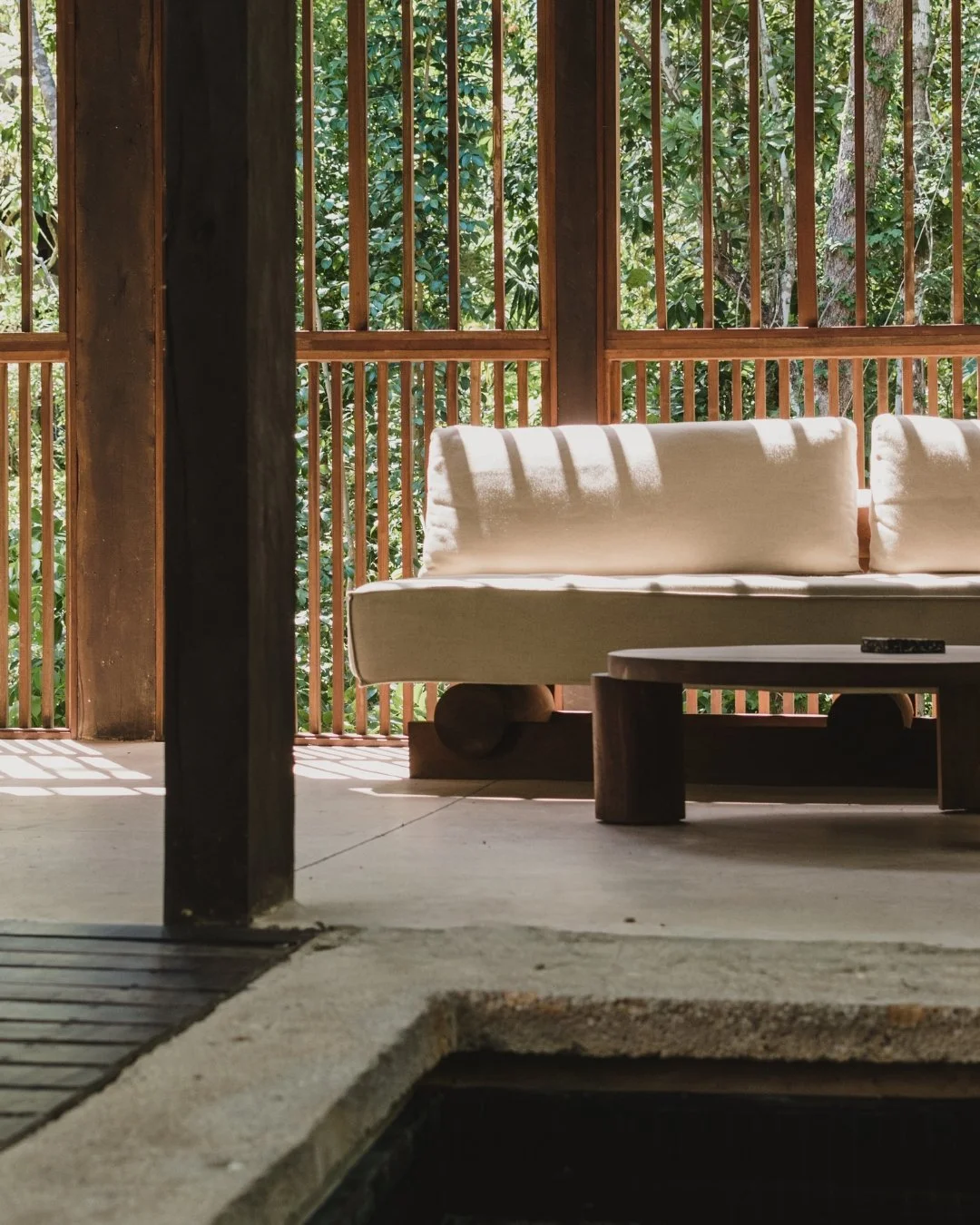 Leather sofa with beige cushions in front of wooden lattice wall with greenery outside.