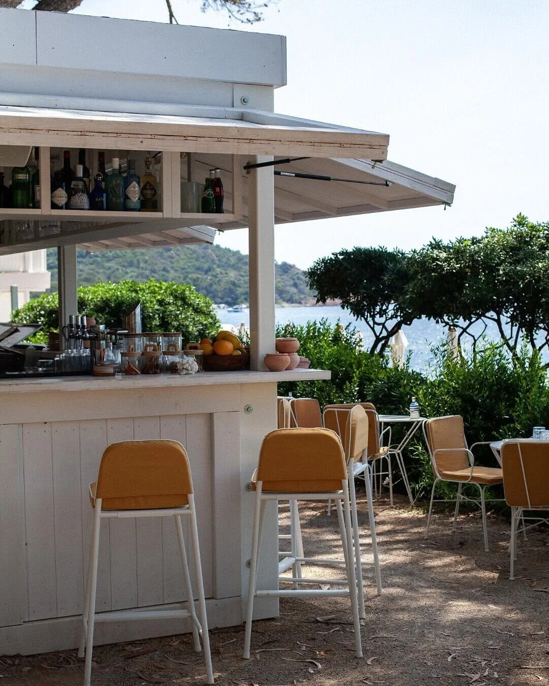 An outdoor bar with yellow chairs, a white counter, and a scenic view of trees and water beyond.