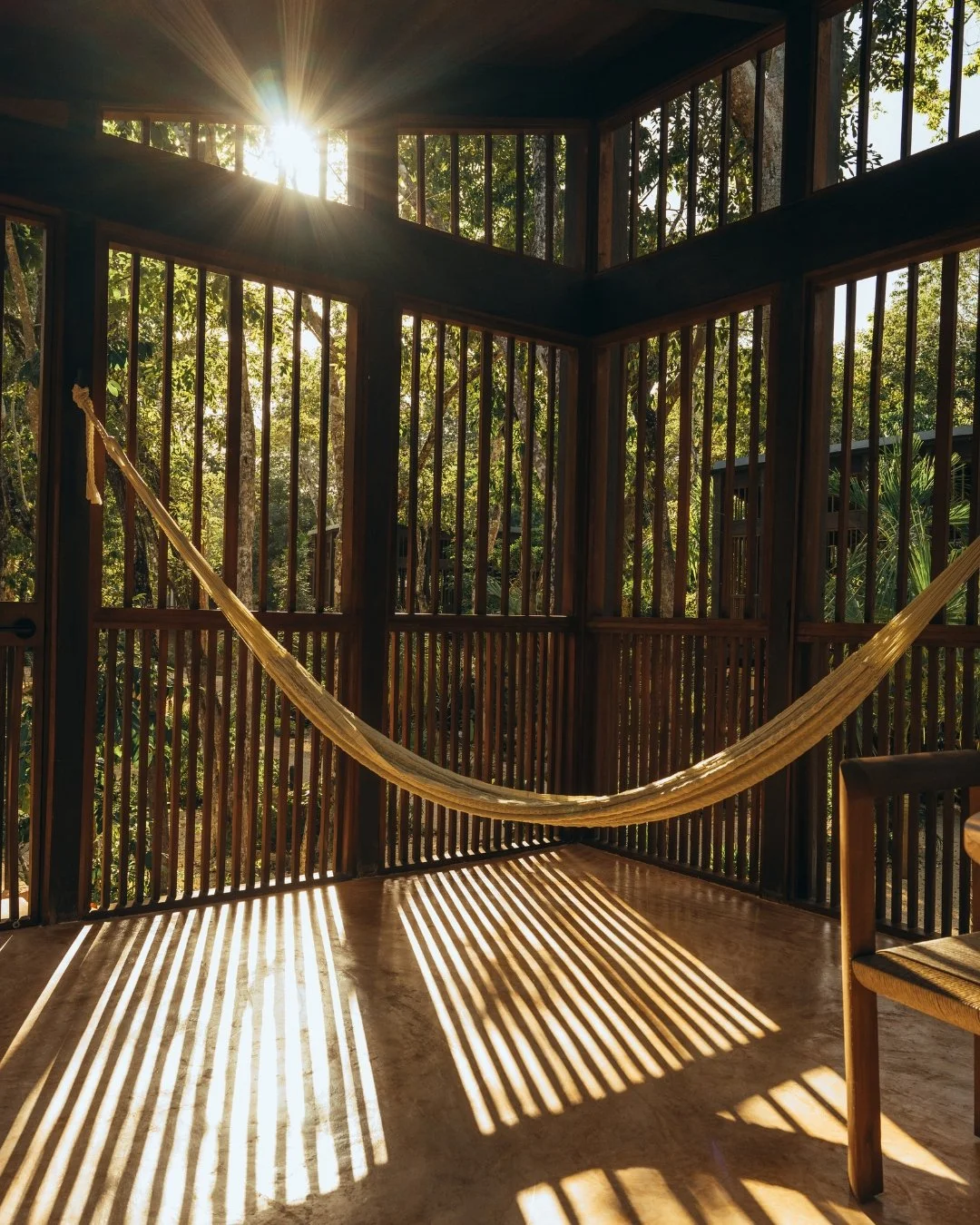 Sunlight streaming through large window panels in a wooden enclosed balcony with a hammock hanging inside