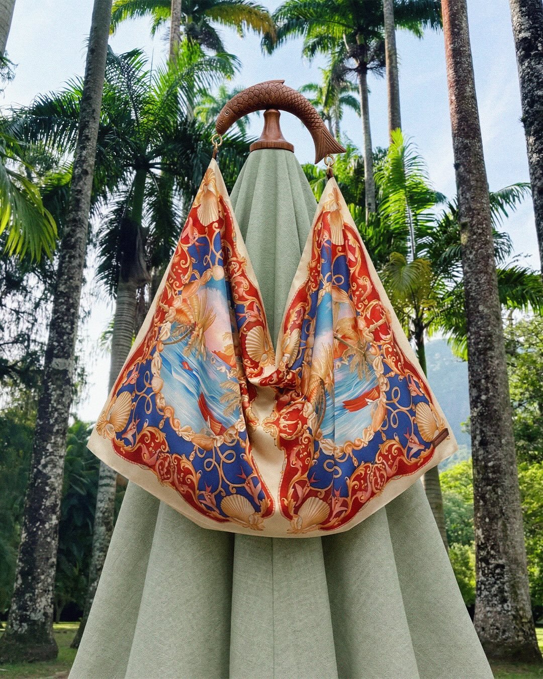 Colorful patterned scarf with nautical and ocean motifs displayed on a green parasol against a backdrop of tropical palm trees.