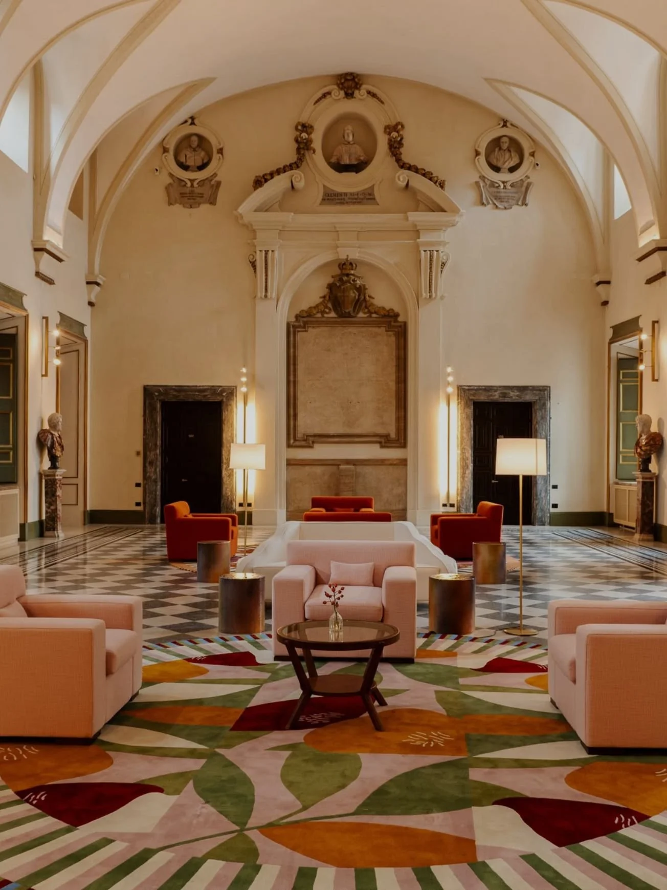 Elegant hotel lobby with high ceilings, soft lighting, contemporary furniture, a colorful patterned carpet, and classical architectural details.