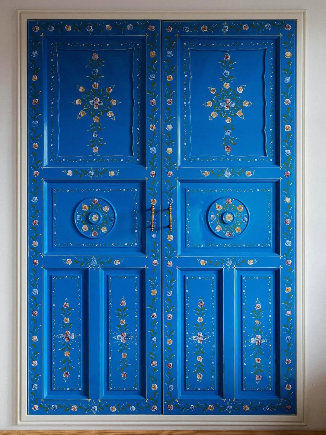 Bright blue double doors with floral patterns and decorative designs, featuring gold handles.