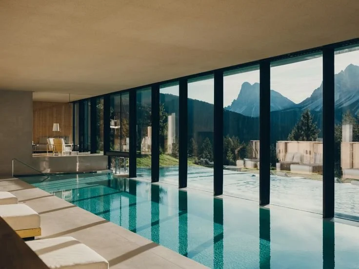 Indoor swimming pool with large floor-to-ceiling windows showcasing mountain and forest views.
