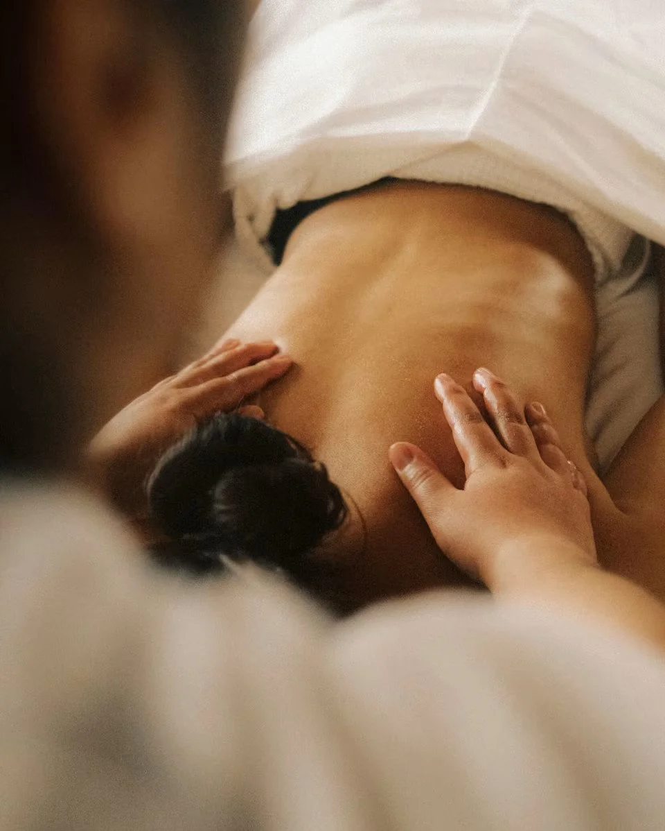 A person receiving a massage on their back, with hands gently pressing on their shoulders and lower back.