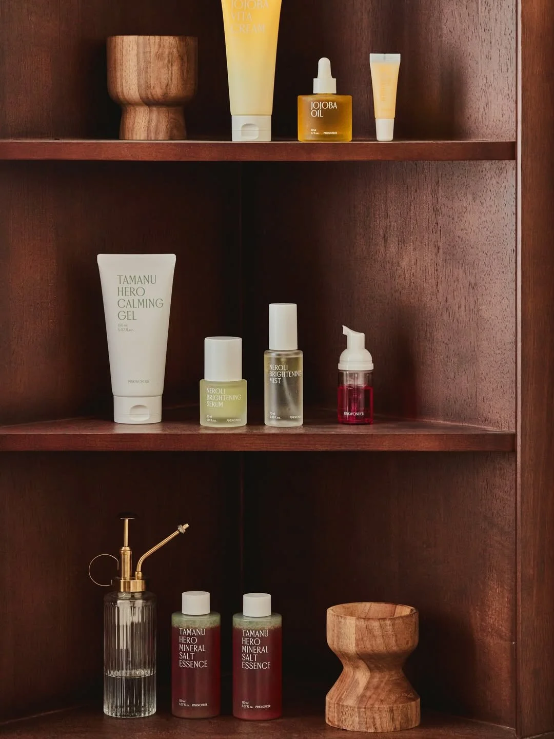 Bathroom shelf with skincare products, wooden bowls, and a glass spray bottle.