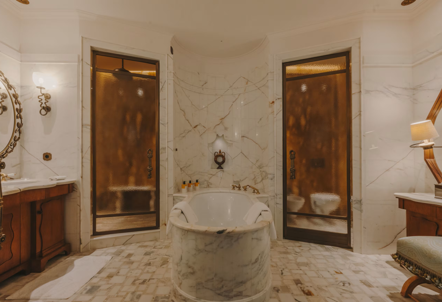 Luxurious marble bathroom with a bathtub, two shower stalls, wooden vanity, and TV, decorated in a classic style with warm lighting.