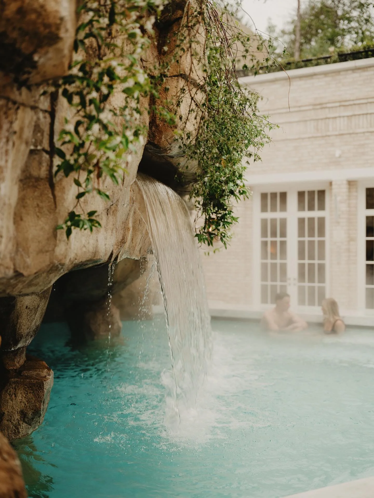 People relaxing in a hot tub with a waterfall feature in a backyard.