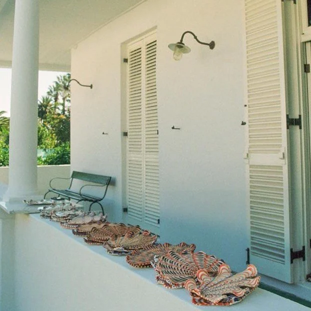Porch with three outdoor lights, white shutters, a bench, and colorful striped fabric or cushions laid out on a ledge.
