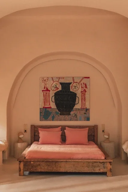A bedroom with a wooden bed, pink bedding, and two pink pillows. There are two bedside tables with lamps. An arched alcove features a large, framed ancient-style vase and decorative art above the bed.