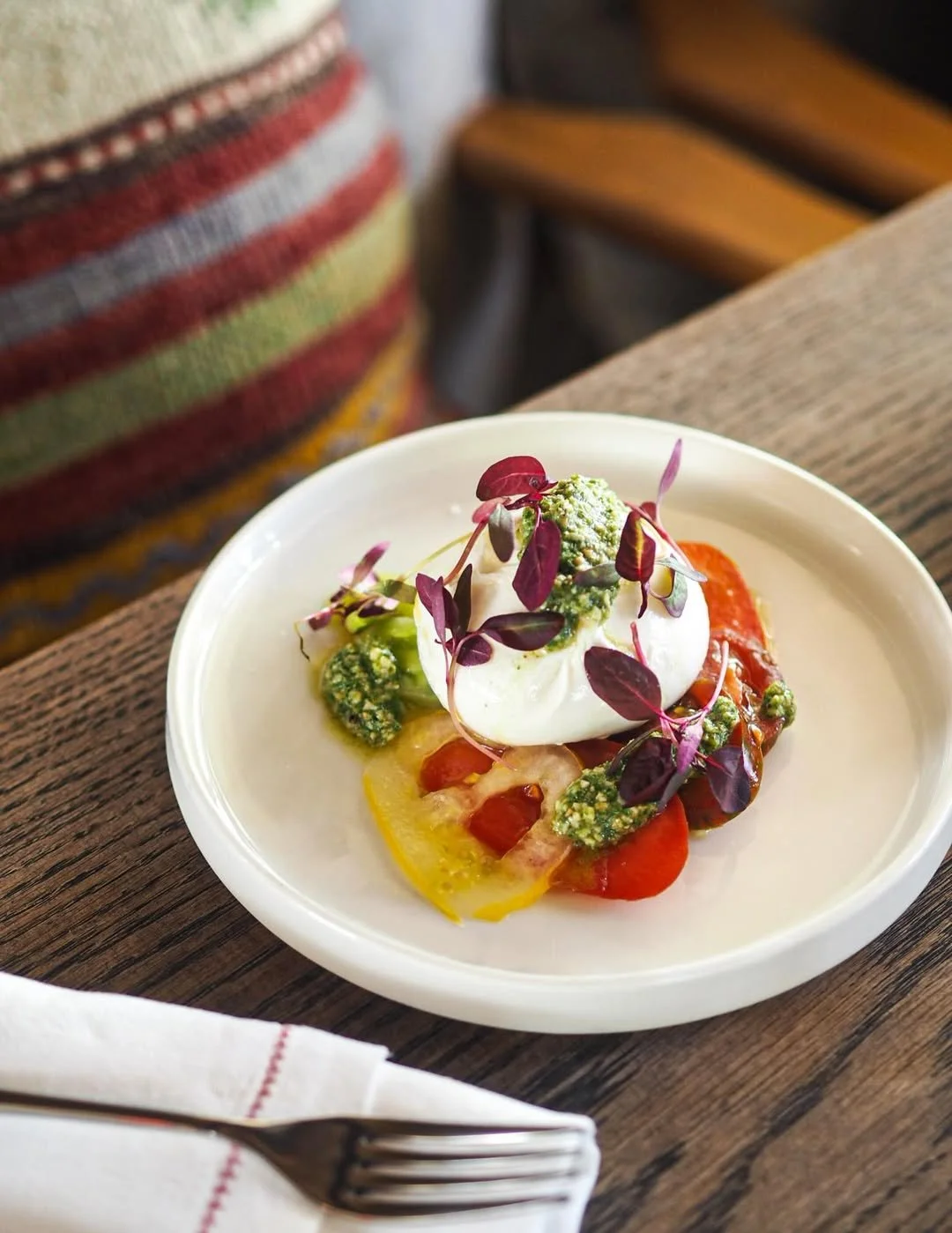 Plate of colorful gourmet salad with cherry tomatoes, broccoli, microgreens, and a dollop of creamy white sauce, served on a white dish.