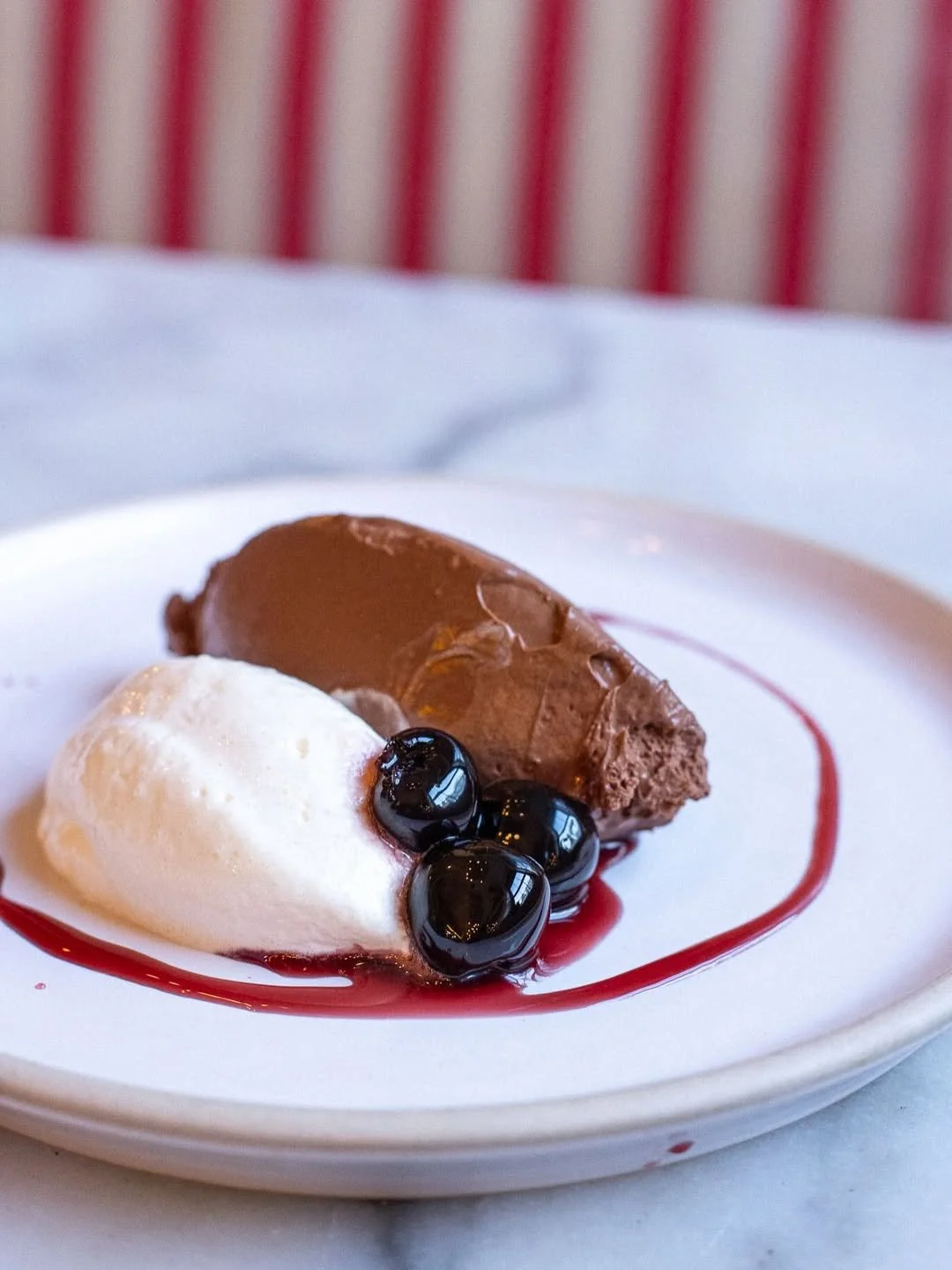 A white plate with a scoop of white ice cream, a dollop of chocolate mousse, and black tapioca pearls, garnished with red sauce.