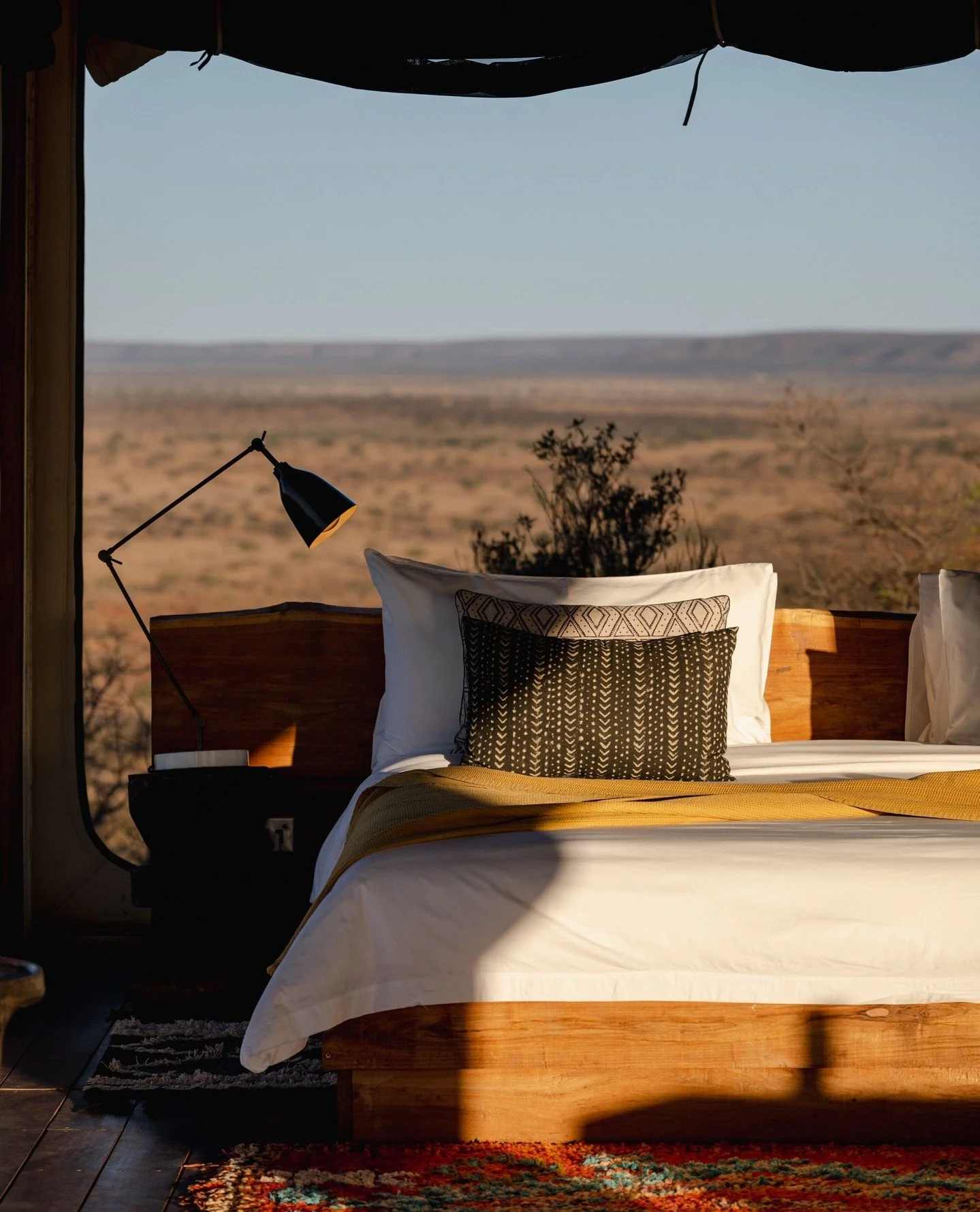 A bed with white linens and decorative pillows in a room with large windows overlooking a desert landscape.