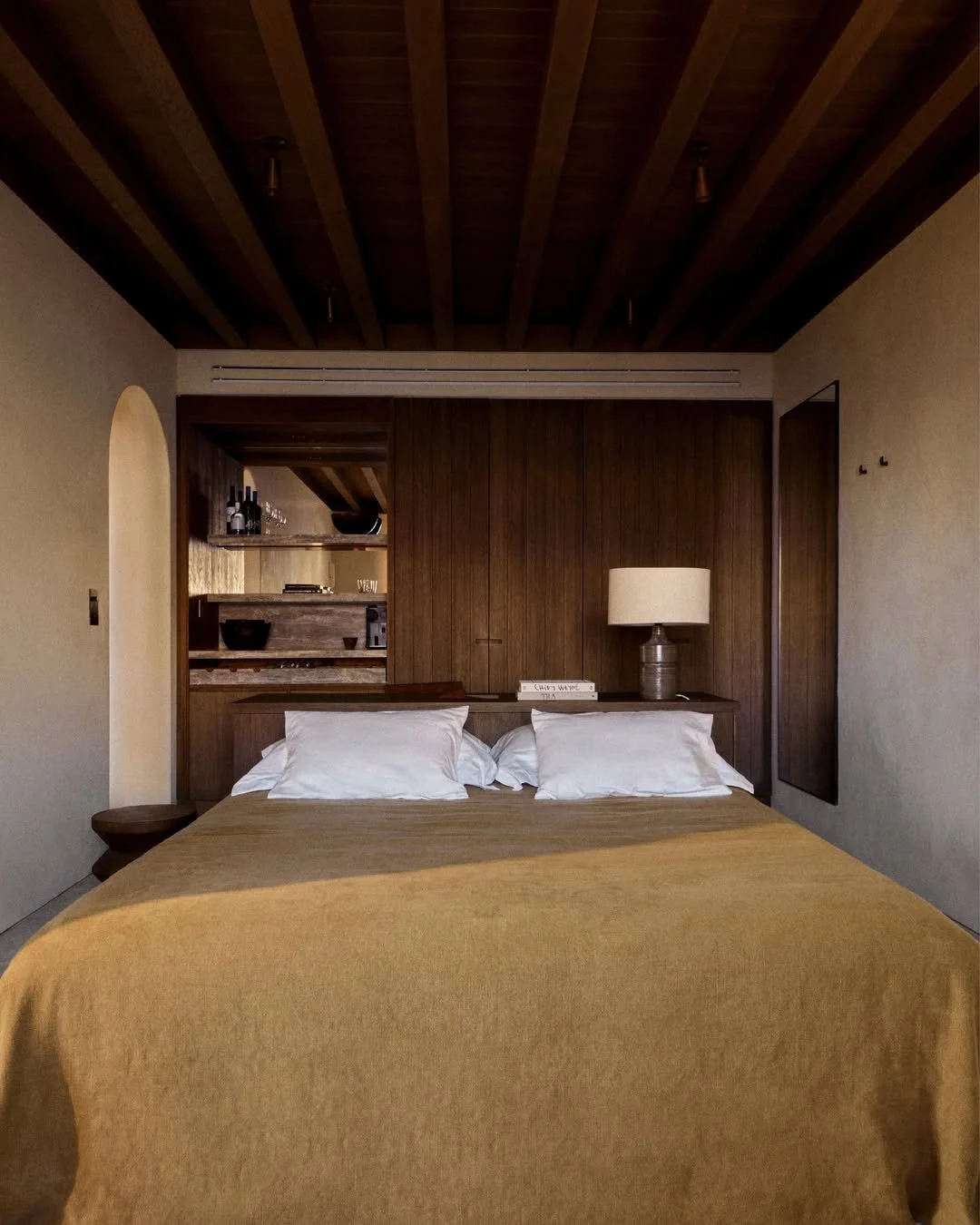 A neatly made bed with white pillows and a mustard-colored blanket in a cozy bedroom featuring wood accents on the headboard, ceiling, and built-in wall paneling.